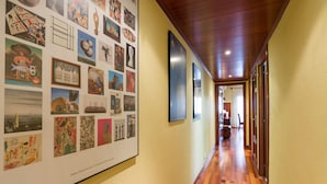 Un couloir doté d’un plancher en bois, d’un mur orné de divers tableaux encadrés et d’un plafond pourvu d’un éclairage encastré.