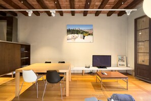 A modern living room with a wooden dining table, two chairs, a TV, and a bookshelf. - GRACIA DREAM, very nice restored vacation rental apartment in Barcelona center, Gracia (Barcelona)