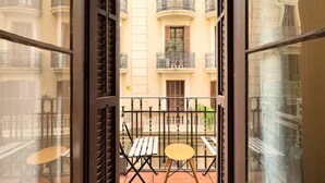 Blick vom Balkon mit Tisch und Stuhl auf einen Innenhof mit Gebäuden und einem Zaun.