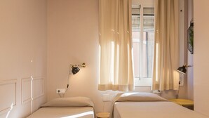 Een kamer met twee eenpersoonsbedden, een kleine tafel, een lamp en een raam met gordijnen.