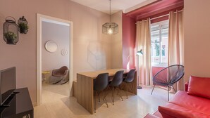 Een moderne woonkamer met een houten eettafel, zwarte stoelen, een rode bank en een hanglamp.