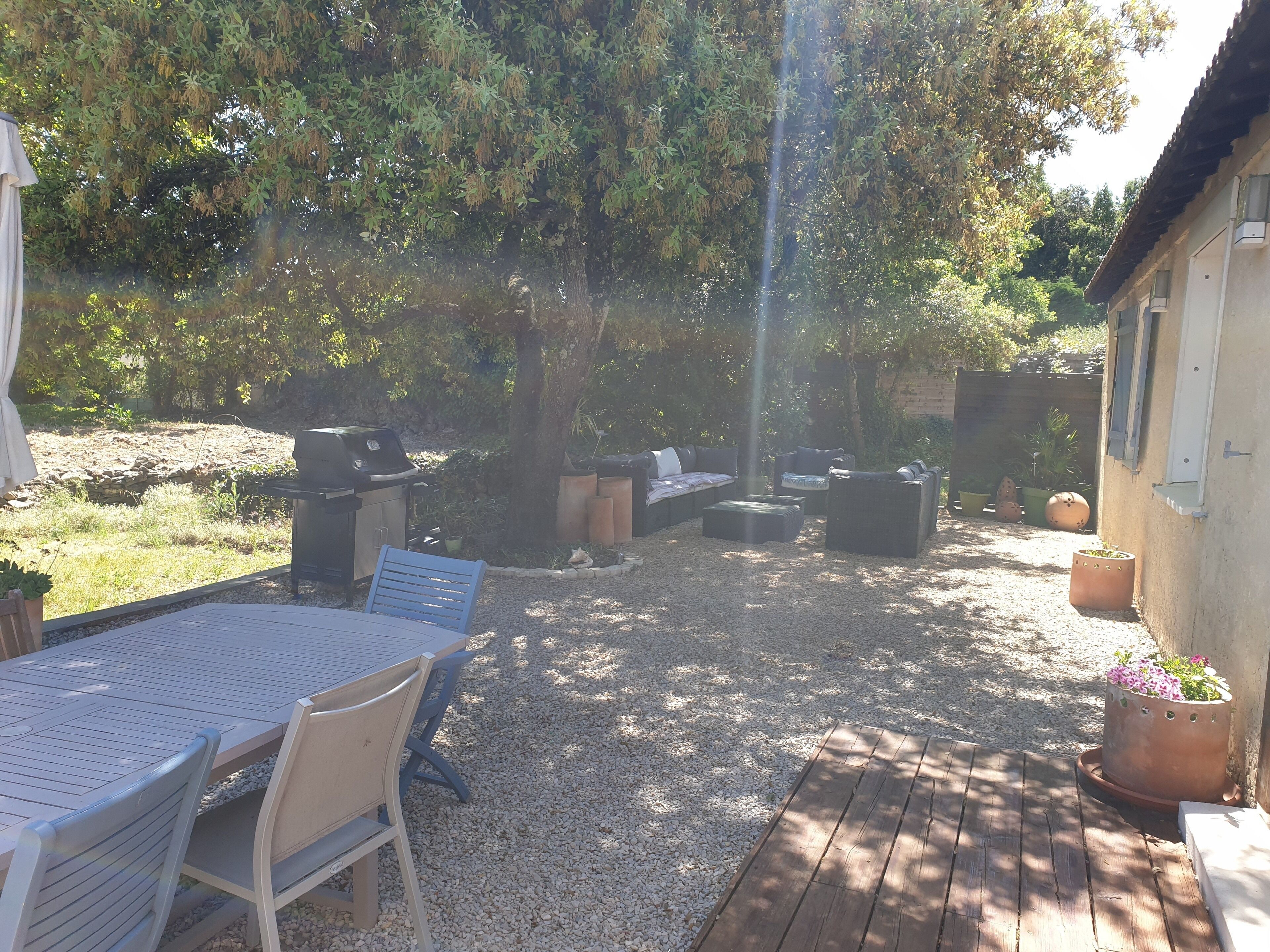 Ein Außenbereich mit einer Terrasse, einem Tisch und Stühlen, einem Grill und einer Sitzecke mit Sofas und einem Couchtisch.