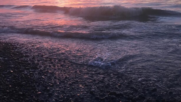 En strand ved solnedgang med bølger der slår ind mod kysten.