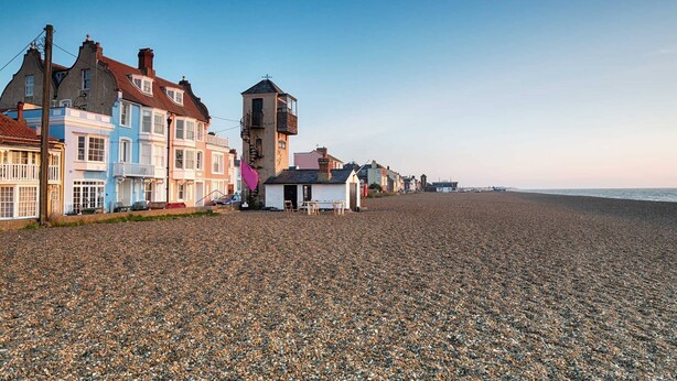 A pebbled beach with colorful seaside cottages and a small tower structure.