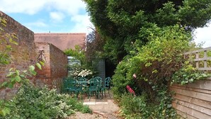 A garden with a gravel path, green metal chairs, and a brick wall.