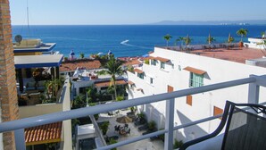 Un balcón con vista al mar, una terraza con mobiliario exterior y un edificio blanco con tejados rojos.