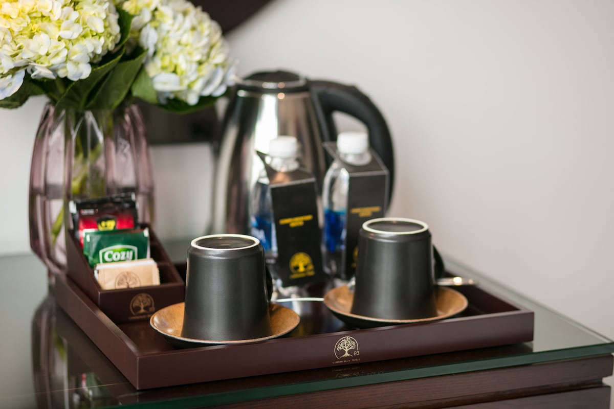 Un plateau avec deux tasses noires, une théière en argent et un vase en verre contenant des fleurs blanches.