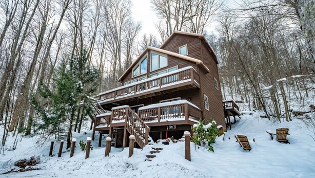 Un chalet à plusieurs étages, doté de balcons et d’une façade en bois, entouré d’une forêt enneigée.