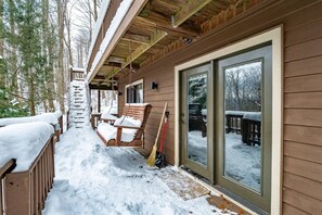 Une cabane en bois dotée d’un porche couvert, d’une porte-fenêtre coulissante et d’une terrasse recouverte de neige.