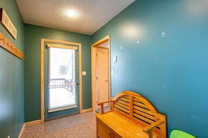 Un couloir avec un banc en bois, une porte et une fenêtre avec des stores.