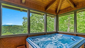 Un bain à remous dans un chalet en bois doté de grandes fenêtres et offrant une vue sur la forêt.