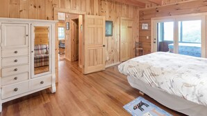 Une chambre aux murs lambrissés, comprenant un lit, une commode et une porte donnant sur une autre pièce.