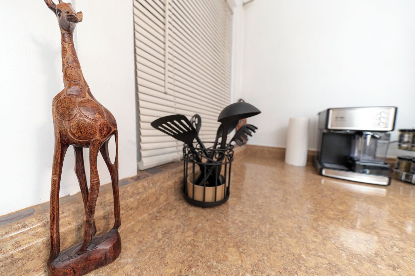 A kitchen with a wooden giraffe sculpture, a coffee machine, and a utensil holder.