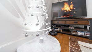 A living room with a TV on a wooden stand, a white Christmas tree, and a fireplace.