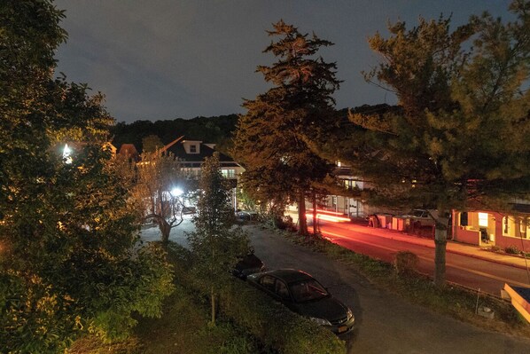 Vista nocturna de una calle residencial con casas, árboles y automóviles estacionados.