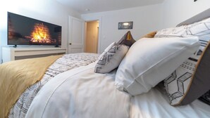 A bedroom with a TV displaying a fireplace, a bed with patterned bedding, and a door leading to another room.