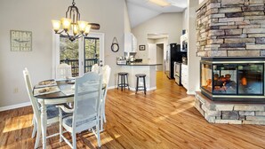 Une salle à manger spacieuse avec un plancher en bois, un lustre et une cheminée en pierre.