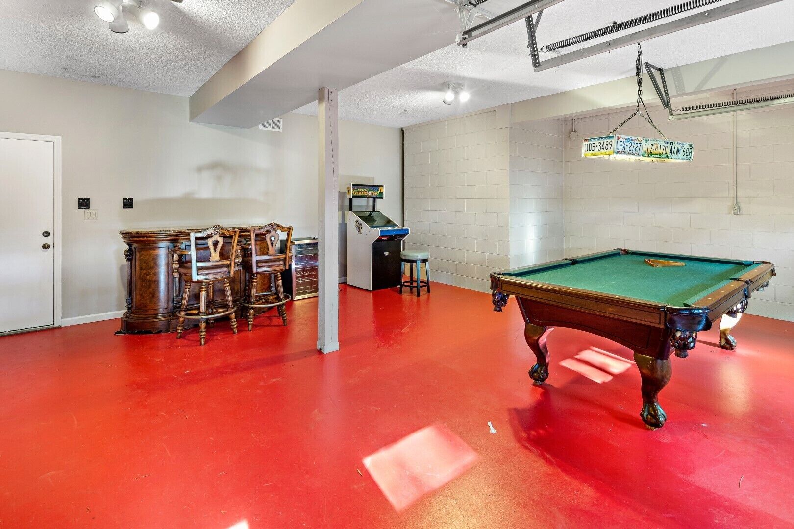A pool table with a red floor, a pool table with a green felt top, and a bar area with stools.