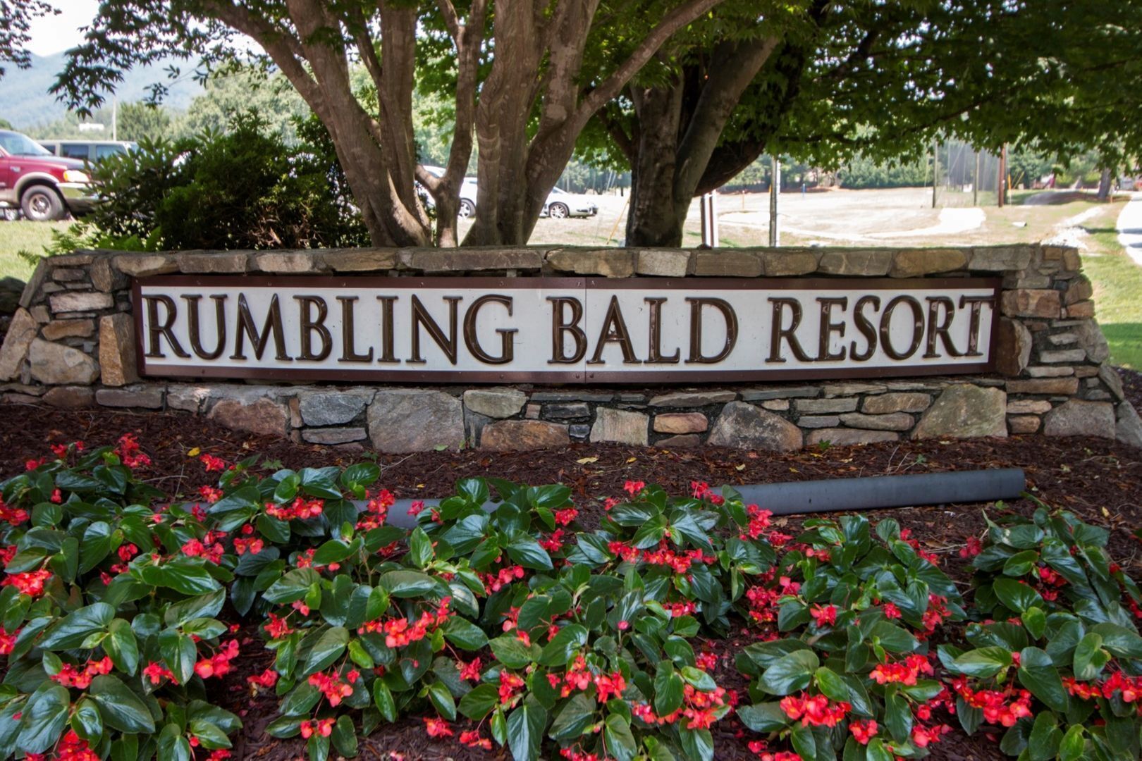 A sign for Rumbling Bald Resort surrounded by a stone wall and red flowers.