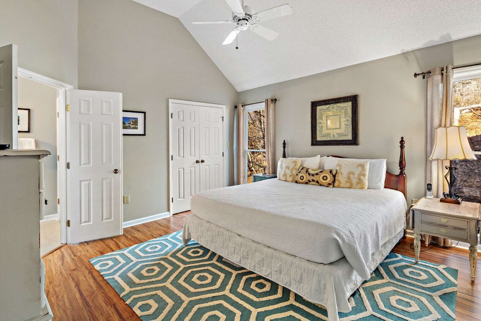 A bedroom with a bed, a ceiling fan, a window with curtains, and a door.