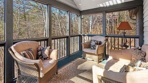 Une véranda avec de grandes fenêtres, des meubles en osier et un ventilateur de plafond.
