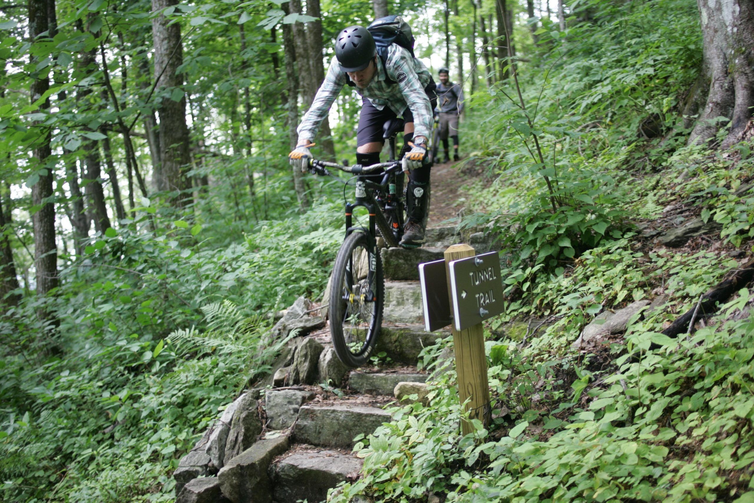 Ein Mountainbiker auf einem steinigen Pfad, umgeben von dichtem Wald.