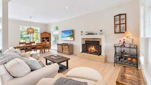 A spacious living room with a fireplace, a dining area, and a view of the outdoors. - Secluded Wainscott Estate with Heated Pool, Hot Tub, Expansive Yard &... (Wainscott)