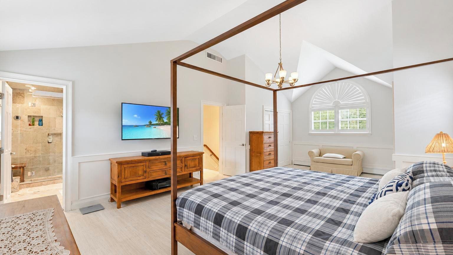A bedroom with a four-poster bed, a television, a wooden dresser, and a window with a view.