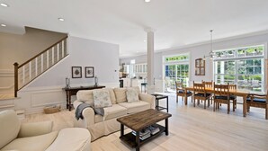Uma sala de estar ampla com escada, conjunto de jantar e vista para o exterior.