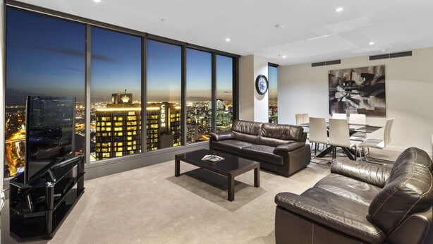Un salon moderne offrant une vue imprenable sur la ville, avec des meubles en cuir et un coin repas comprenant une table et des chaises.