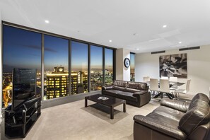 Uma sala de estar moderna com uma grande vista da cidade, móveis de couro e uma área de jantar com mesa e cadeiras.