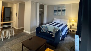 A hotel room with a bed, a desk, a chair, a small table, and a closet. - The Westmoor (Toledo)