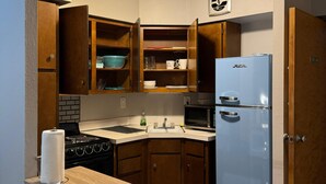 A compact kitchen with wooden cabinets, a built-in microwave, a refrigerator, and a small countertop with a paper towel holder. - The Westmoor (Toledo)