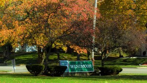 A sign for 'The Westmoor' apartments with a clear view of autumn-colored trees in the background. - The Westmoor (Toledo)