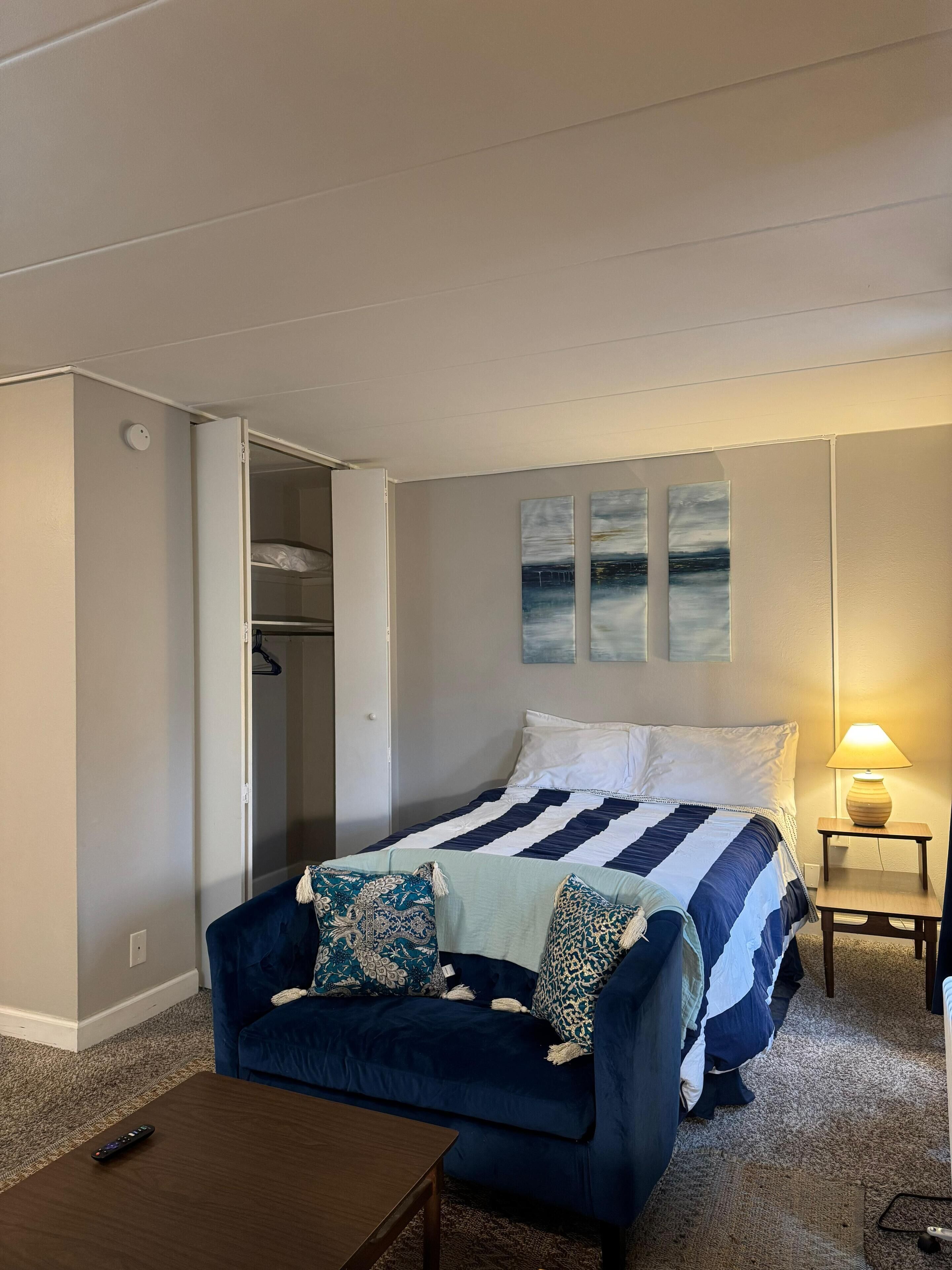 A bedroom with a bed, a blue sofa, a bedside table with a lamp, and a closet.