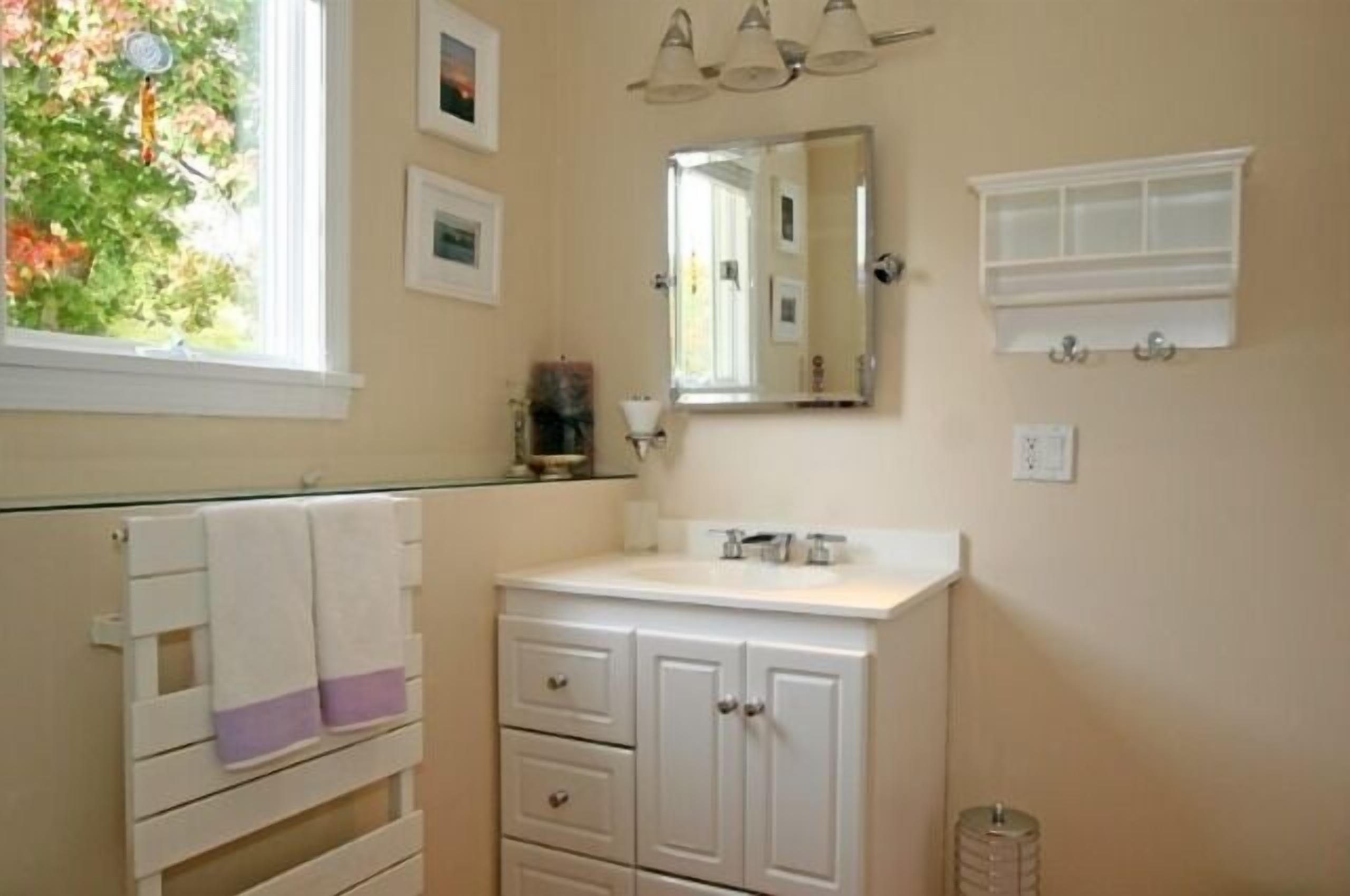 A bathroom with a white vanity, a mirror, and a window with a view of trees.