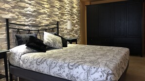 A bedroom with a stone wall, a bed with patterned bedding, a bedside table with a lamp, and a dark wardrobe. - The only one with a pool in downtown Tossa. Beach 100 m away, sleeps 6, Wi-Fi, renovated (Tossa de Mar)