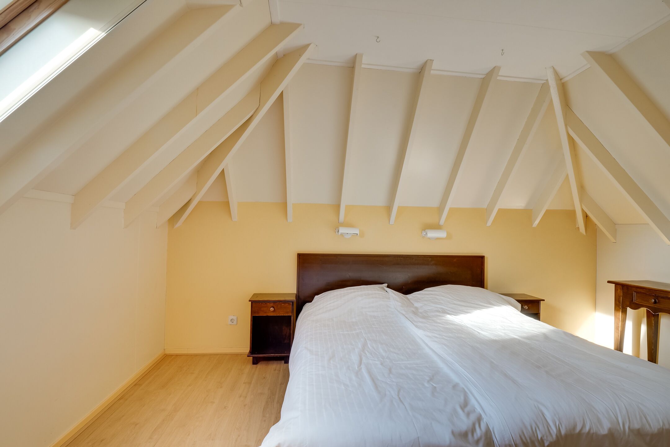 A bedroom with a sloped ceiling, a wooden headboard, a large bed, and two bedside tables.
