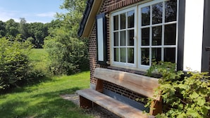 Une maison en briques avec une grande fenêtre et un banc en bois à l’extérieur.