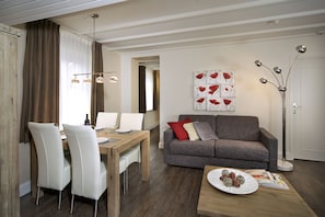 A modern living room with a dining area, a grey sofa, and a coffee table with pastries.