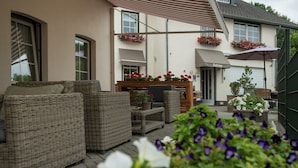 An outdoor seating area with wicker furniture, a wooden table, and flower planters. - Bergkristal, premium apartment located in Epen - South Limburg. (Epen)