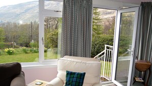 A room with a white armchair, a brown sofa, and a small wooden table. - Quiet location with stunning views, sleeps 8, pet friendly, free Wi-Fi (Cairndow)