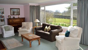 A cozy living room with a fireplace, a coffee table, and a view of the garden through large windows. - Quiet location with stunning views, sleeps 8, pet friendly, free Wi-Fi (Cairndow)