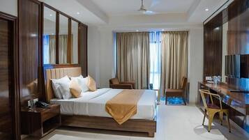 A hotel room with a large bed, a desk, a chair, and a wardrobe.