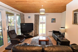 A living room with a TV, leather sofas, a coffee table, and a wooden ceiling. - Stunning location with sea and hill views, close to resort facilities (Hunters Quay)
