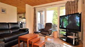 A living room with a black leather sofa, a wooden coffee table, a brown recliner, and a TV on a black stand.