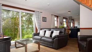 A living room with a leather sofa, glass coffee table, and a view of the outdoors. - Lovely cottage with loch views, near Dunoon, sleeps 6 (Blairmore)