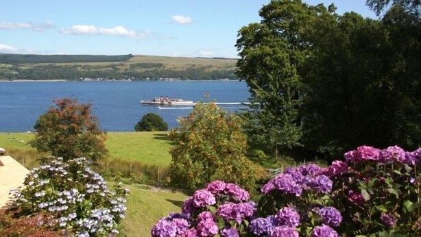 A lake with a boat, surrounded by greenery and purple flowers. - Lovely cottage with loch views, near Dunoon, sleeps 6 (Blairmore)