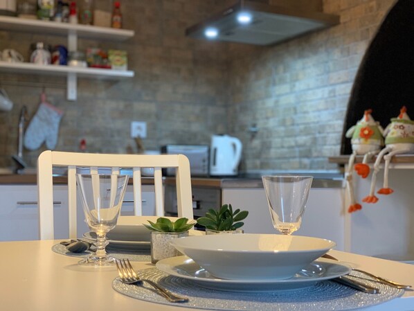 A dining table set with a white plate, two clear glasses, a fork, and a knife. There is a small potted plant on the table. - Rustic and romantic house fully renovated with private garden for couples (Feteiras)