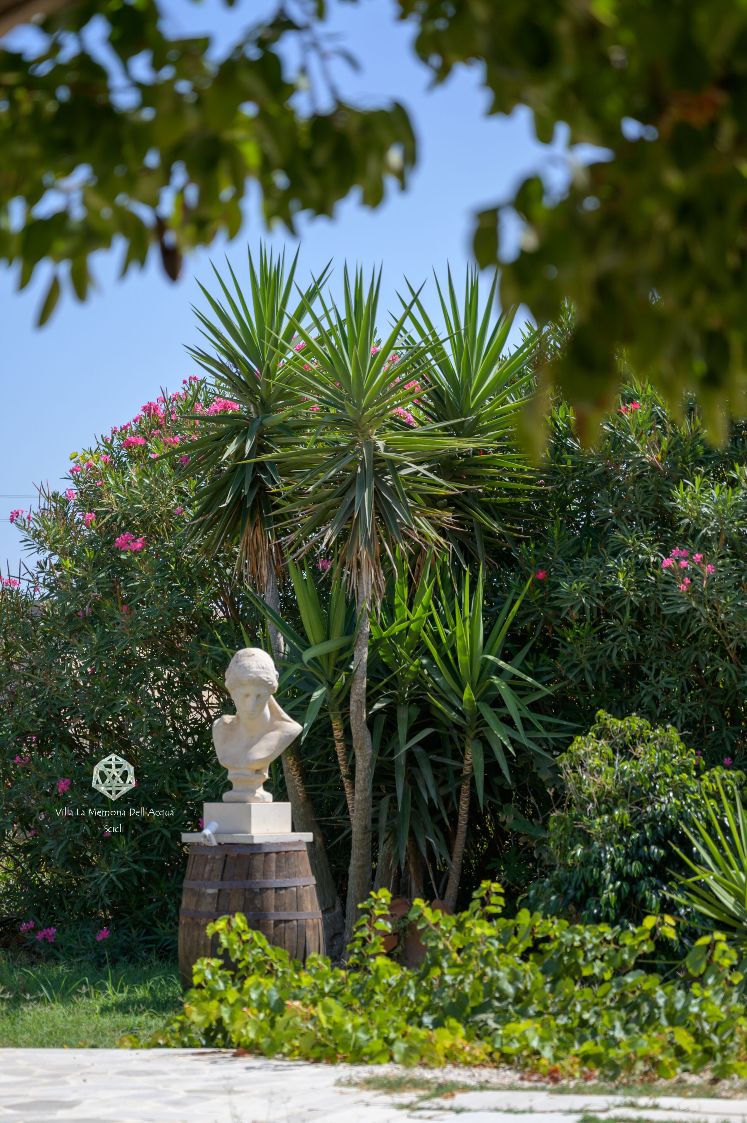 Eine Skulptur auf einem Sockel in einem Garten mit verschiedenen Pflanzen und blauem Himmel.